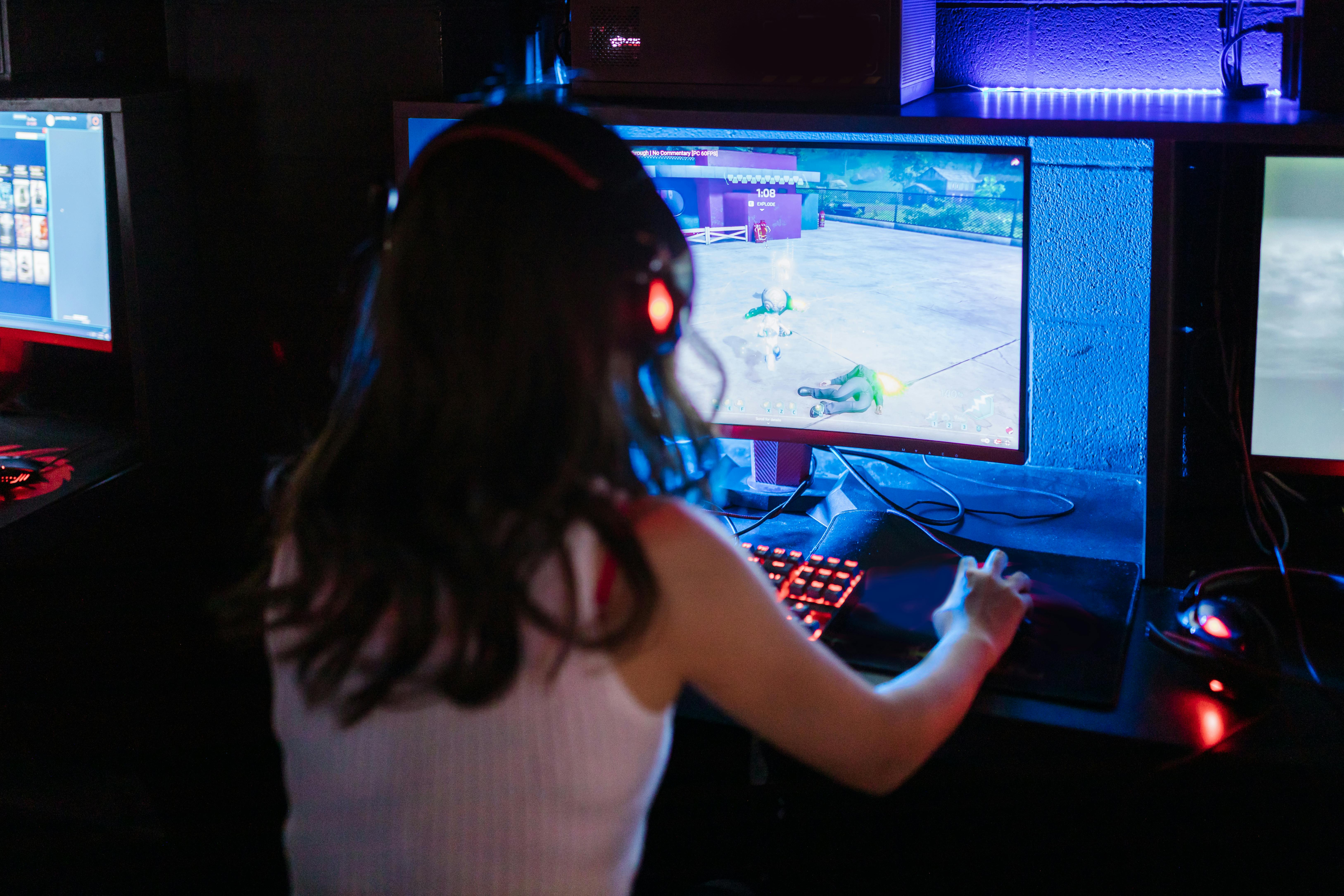 Female gamer focused on playing a competitive online game with RGB keyboard and headphones.